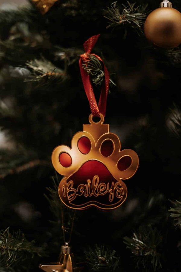 Bola de navidad en forma de huella de perro con el nombre de baileys, en color espejo oro y fondo rojo espejo.